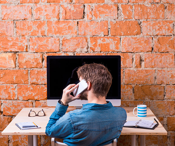 Man on cell phone at desk in front of brick wall